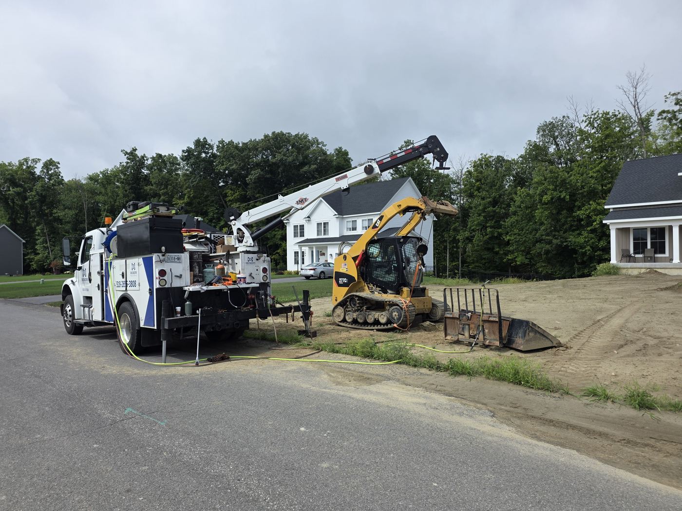Decker's Industrial boom service truck with the crane extended, repairing a compact track loader at a residential job site
