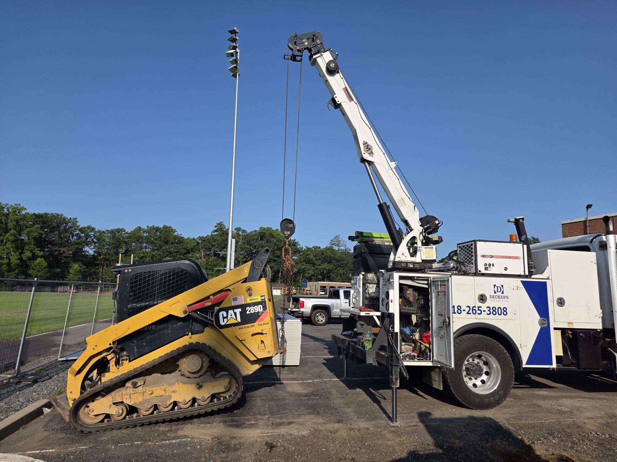 Decker's Industrial boom service truck lifting a component next to a compact track loader on a job site