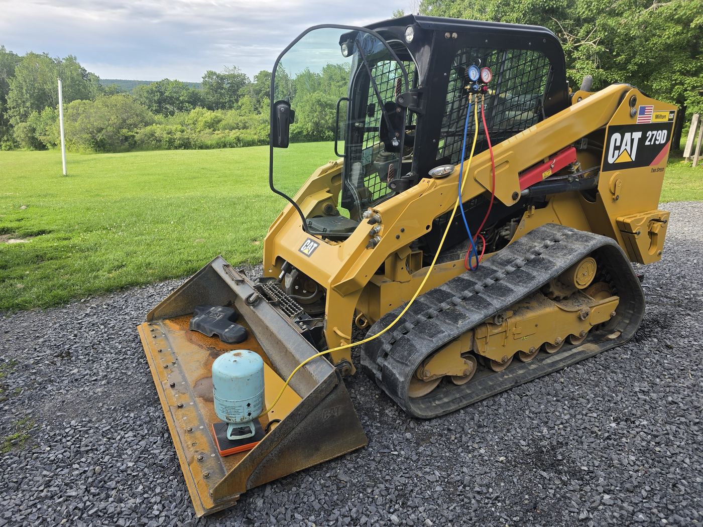 Compact track loader in a field with the engine cover open during a scheduled preventative maintenance service